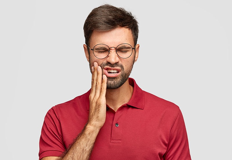 Ein Mann hält schmerzversehrt seine Wange